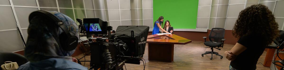 students working in a studio behind the camera filming a news anchor
