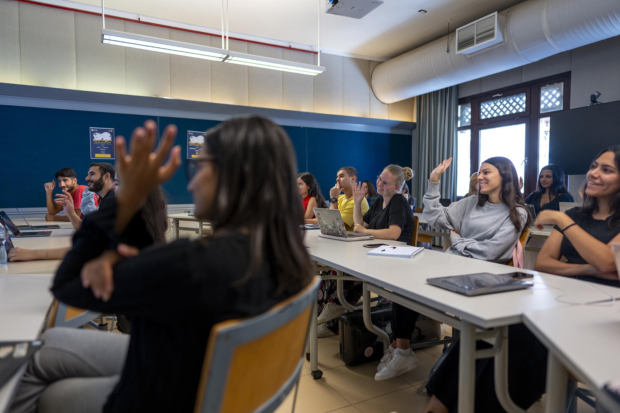 students raising their hands in class room in an interactive class discussion