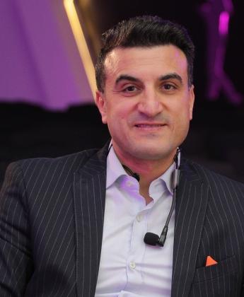  there are headphones hanging from his neck ,A man wearing a suit and sitting on a chair 