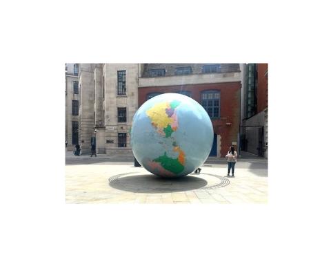 There is a big globe in front of buildings and a woman is standing beside it