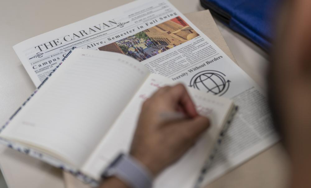 student taking notes in their notebook held above the caravan