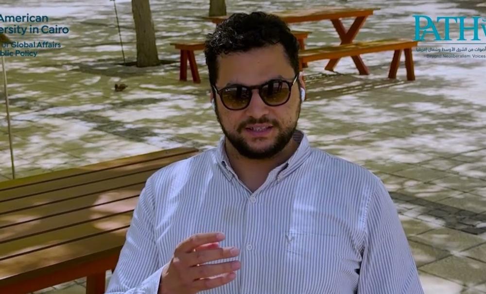 A man is sitting and talking. He is wearing sunglasses
