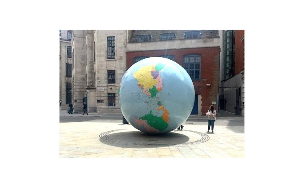 There is a big globe in front of buildings and a woman is standing beside it