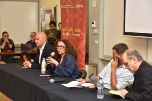 Four people sitting at a panel table. Woman speaking into a microphone.