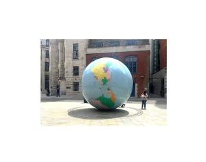 There is a big globe in front of buildings and a woman is standing beside it