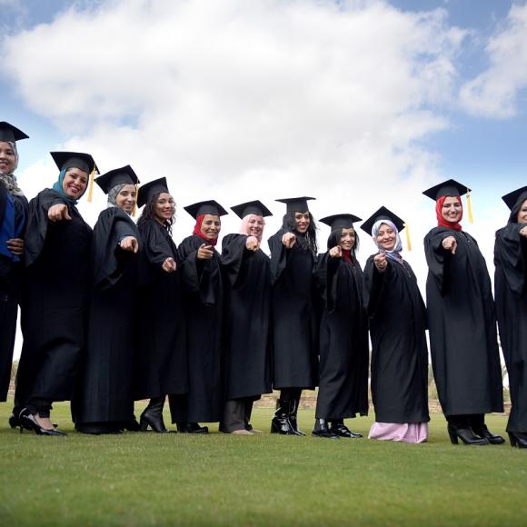 Female graduates wearing their caps and gowns, standing and laughing together 