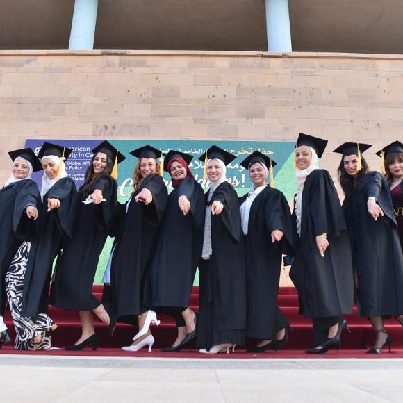 Female graduates wearing their caps and gowns, standing and laughing together 