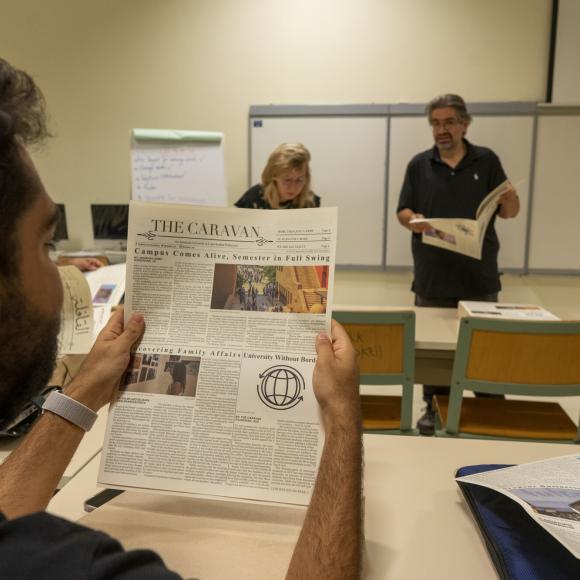 student holding a copy of caravan student newspaper in classroom 